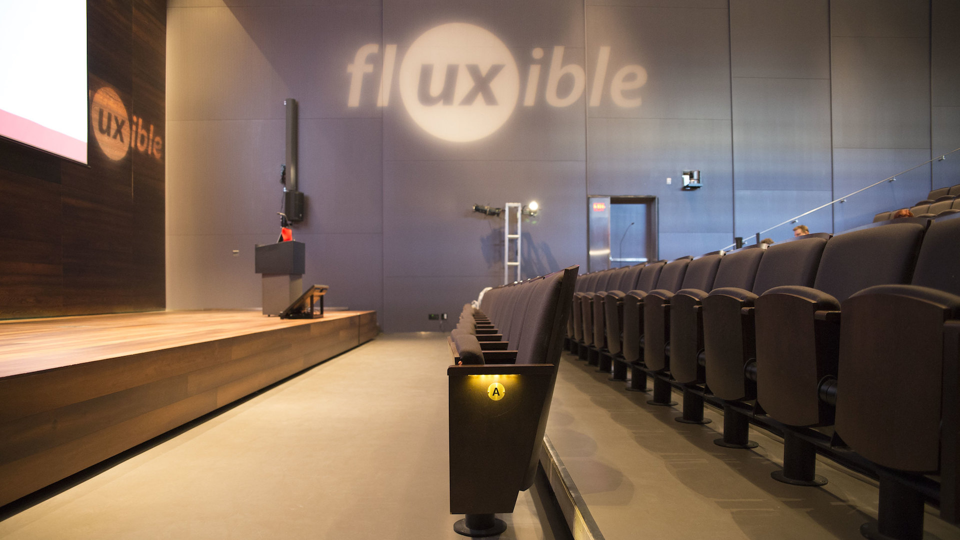 Empty rows of seats in a theatre with the Fluxible logo cast on a grey wall.
